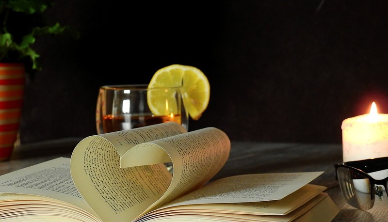 Un libro aperto a forma di cuore, una bevanda, una candela e un'atmosfera intima: un invito al romanticismo e alla riflessione.