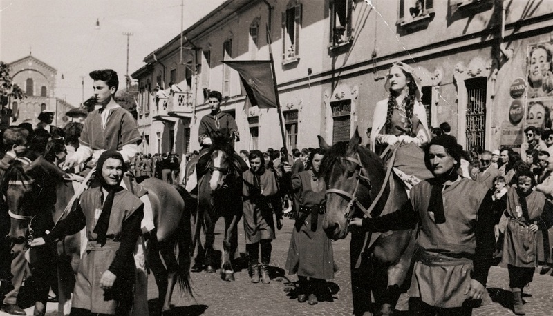 Sfilata storica con persone in costumi tradizionali, a cavallo e a piedi, in un'atmosfera di orgoglio nazionale.