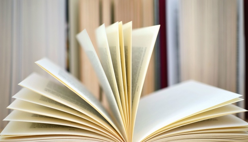 Un libro aperto su uno sfondo di pagine sfocate evoca un'atmosfera di scoperta e lettura profonda.